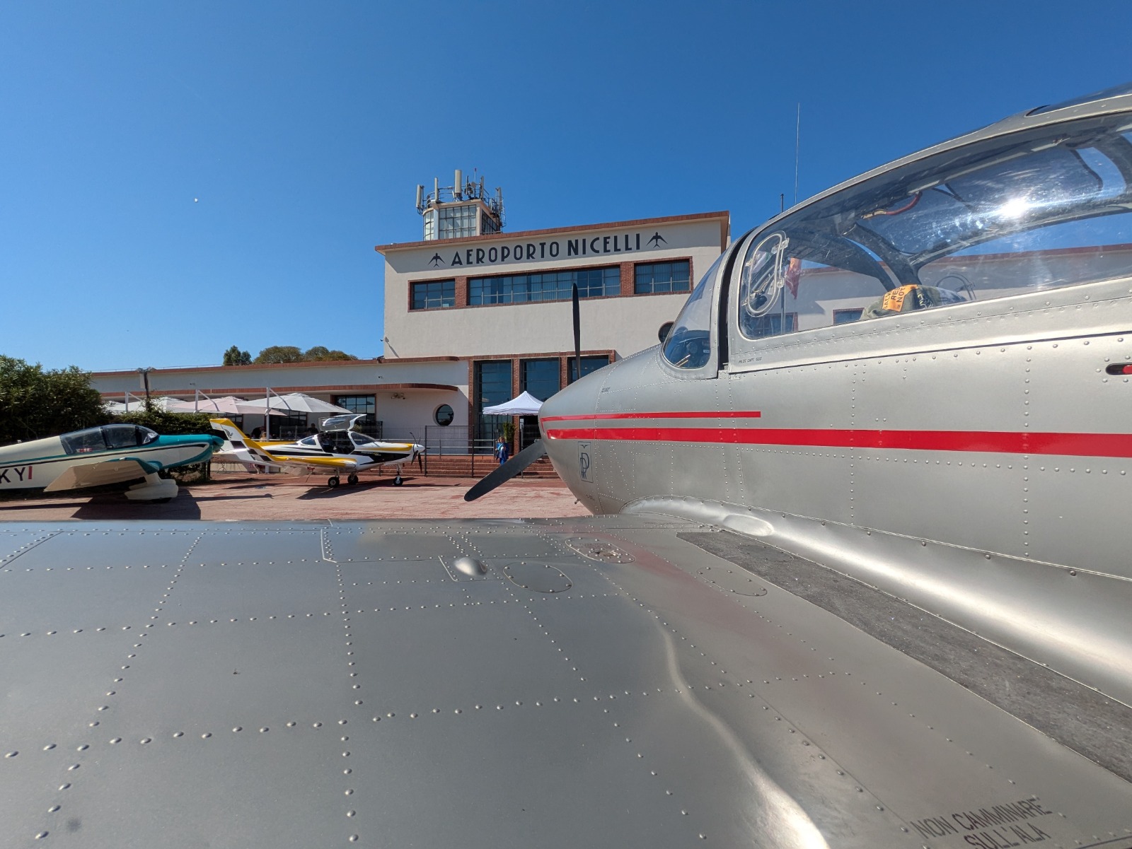 Vista dell'Aeroporto Nicelli con piccoli aerei in sosta e cielo blu sopra.